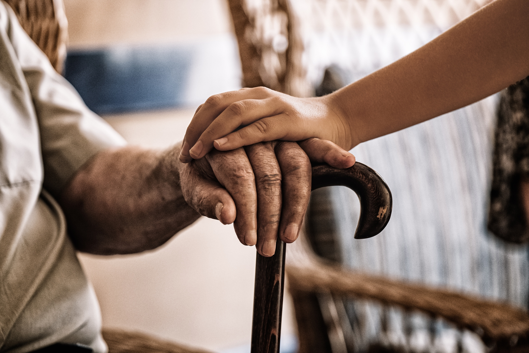 An older person's hand resting on a cane, with a younger hand laid gently on top